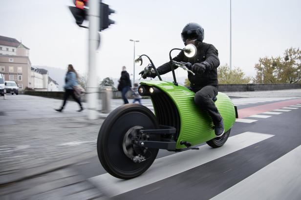 Ein Mann fährt ein ungewöhnliches, grünes Motorrad auf einer Straße.