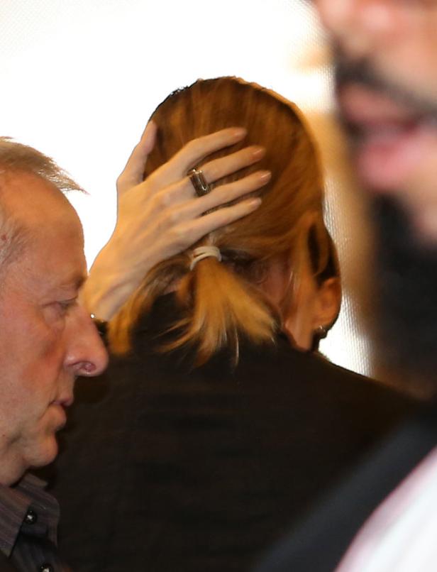 Eine Frau mit blonden Haaren trägt einen Ring und fasst sich an den Kopf.