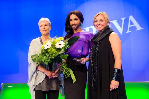 Conchita Wurst mit zwei Frauen bei einer Preisverleihung.
