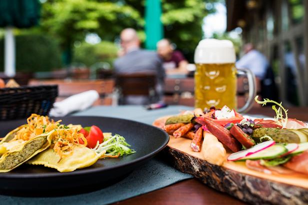 Auf einem Tisch im Freien stehen Maultaschen, eine Wurstplatte und ein Bierkrug.