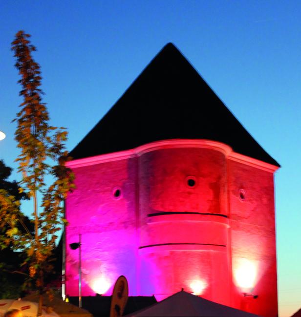 Ein Turm mit einem schwarzen, pyramidenförmigen Dach ist rosa beleuchtet.