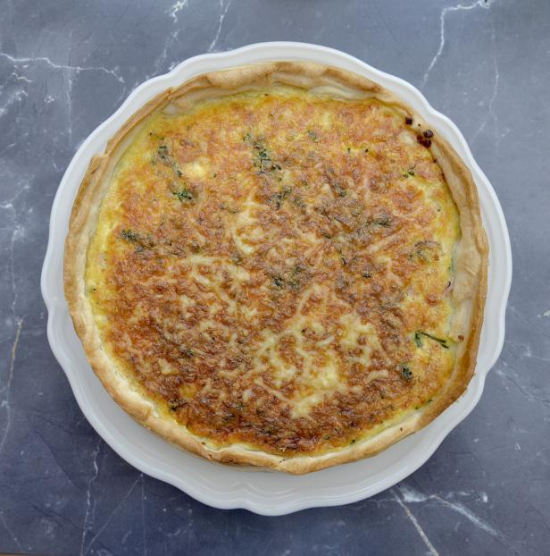 Eine Quiche mit Käse und Kräutern auf einem weißen Teller.