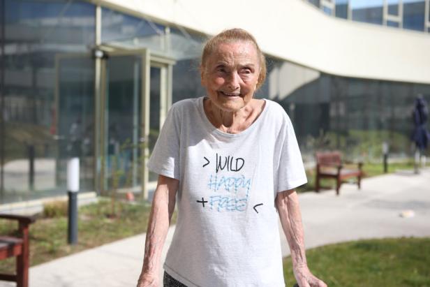 Eine ältere Frau mit einem T-Shirt mit der Aufschrift „Wild Happy + Free“ lächelt.