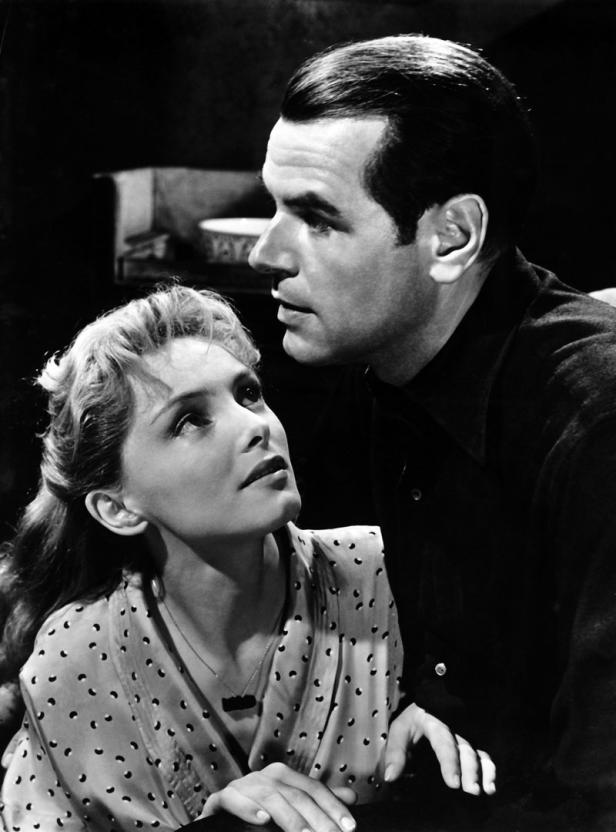 Eine Frau blickt zu einem Mann auf, beide in einem Schwarzweiß-Film-Still.