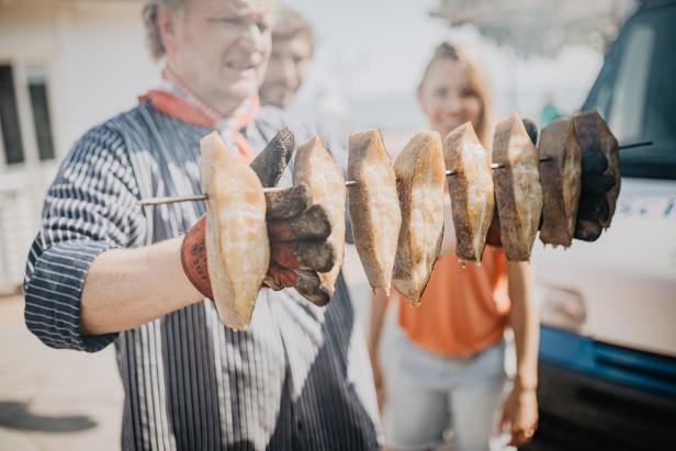 Ein Mann hält einen Spieß mit geräucherten Fischstücken in der Hand.