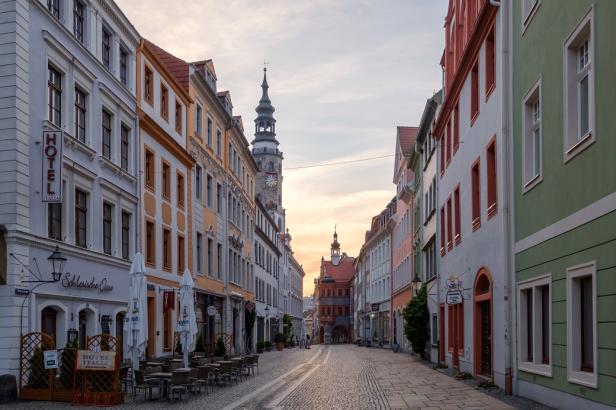 Blick auf eine Kopfsteinpflasterstraße mit historischen Gebäuden und einem Turm im Hintergrund.