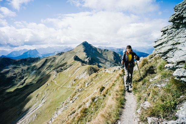 Ein Wanderer geht mit Stöcken auf einem Pfad in den Bergen.