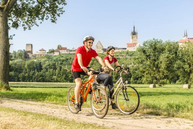 Ein Paar fährt mit Fahrrädern vor der Kulisse einer mittelalterlichen Stadt.