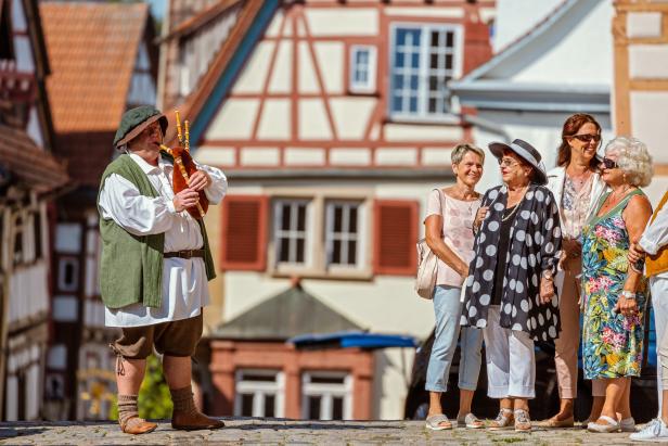 Ein Dudelsackspieler in historischer Kleidung spielt vor einer Gruppe von Frauen in einer Stadt.