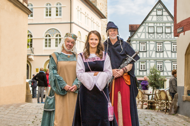Drei Personen in historischen Kostümen posieren in einer Altstadt.