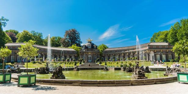 Das Orangerieschloss in Kassel mit einem Teich und mehreren Springbrunnen im Vordergrund.