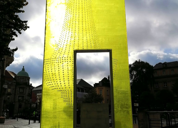 Ein gelbes Kunstwerk mit kleinen Noppen steht in einer Stadt.