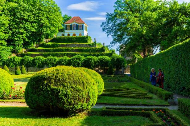 Ein Garten mit kunstvoll geschnittenen Hecken und einem kleinen Haus auf einem Hügel.