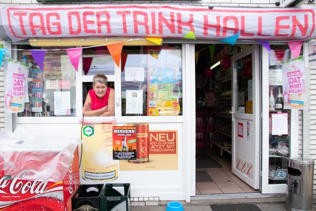 Eine Frau lehnt im Fenster eines Kiosks, der mit „Tag der Trinkhallen“-Bannern geschmückt ist.