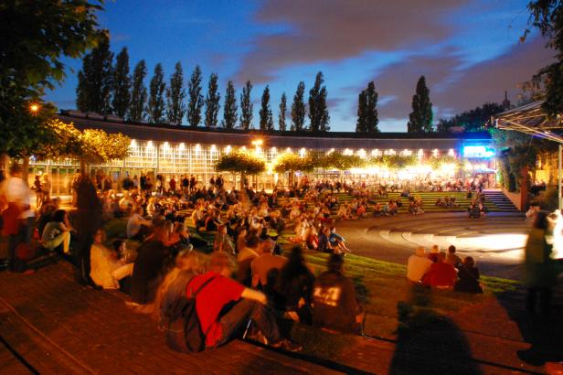 Viele Menschen sitzen abends im Freien auf einer Art Freilichtbühne.