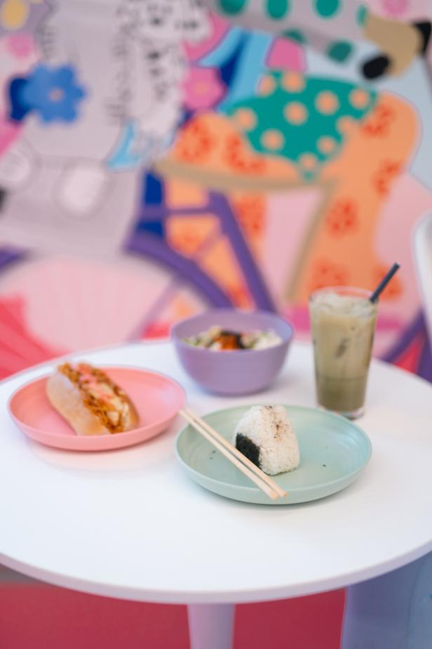 Auf einem Tisch stehen ein Hotdog, eine Schale und ein Onigiri mit einem Getränk.