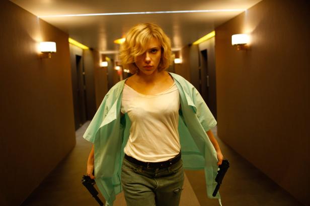 Scarlett Johansson geht mit zwei Pistolen in der Hand einen Hotelflur entlang.