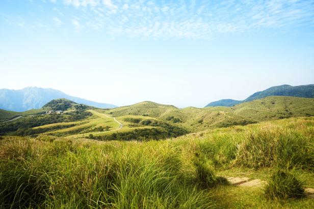 Hügelige Landschaft mit Gras und einem Wanderweg unter blauem Himmel.