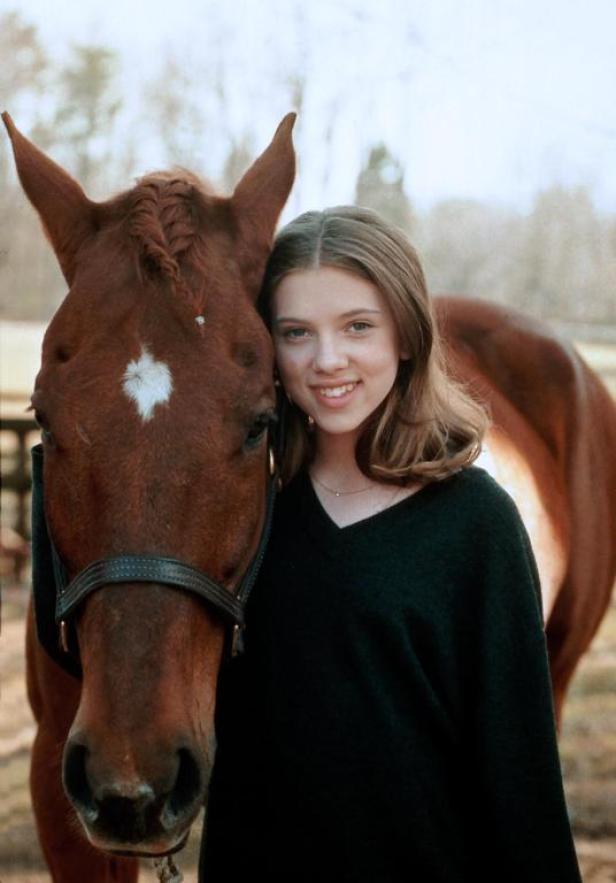 Eine junge Scarlett Johansson posiert mit einem braunen Pferd.