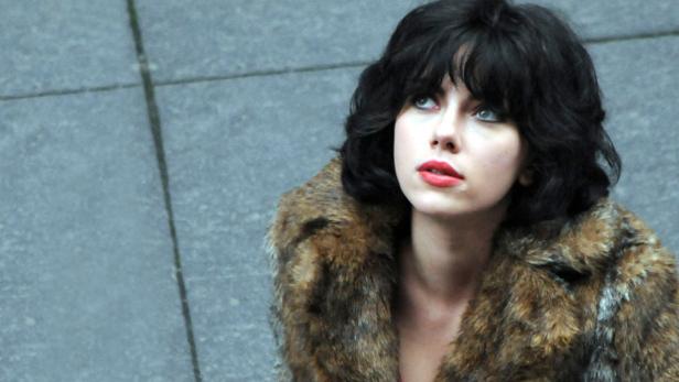 Scarlett Johansson mit dunklen Locken und Pelzmantel blickt nach oben.