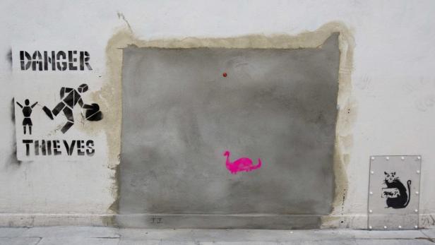 Auf einer Wand befinden sich Graffitis, darunter ein rosa Dinosaurier und eine Warnung vor Dieben.
