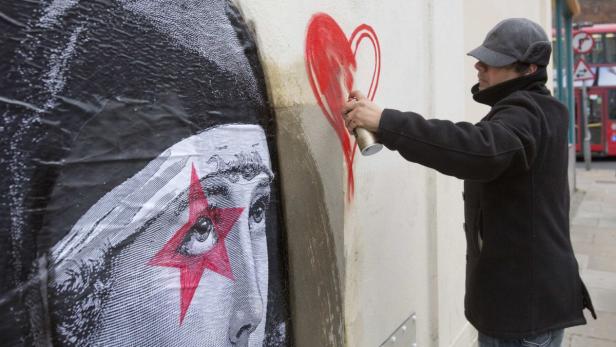 Eine Person sprüht ein rotes Herz neben ein Plakat mit einem Gesicht und einem roten Stern.