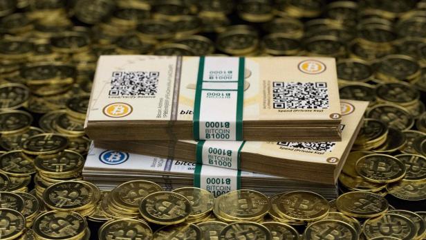 Stapel von Bitcoin-Banknoten und Goldmünzen liegen auf einem Tisch.