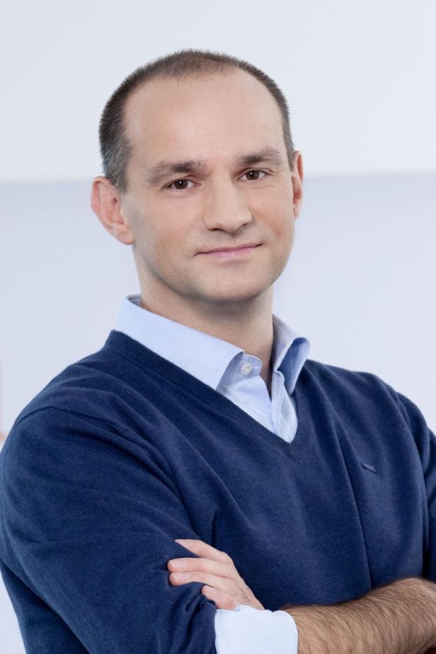 Ein Mann mit blauem Pullover und verschränkten Armen blickt in die Kamera.