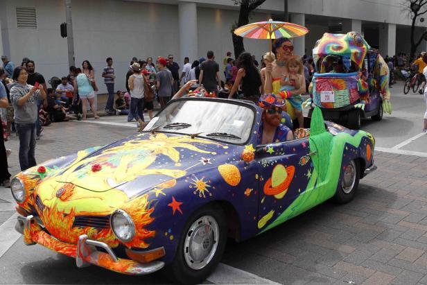 Ein bunt bemaltes Auto fährt in einer Parade mit Zuschauern am Straßenrand.