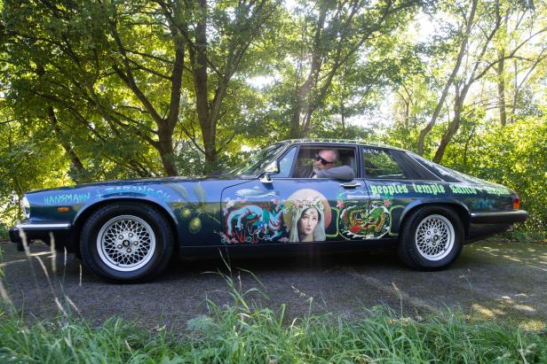 Ein mit Kunst bemalter Jaguar XJS mit einem Mann am Steuer.