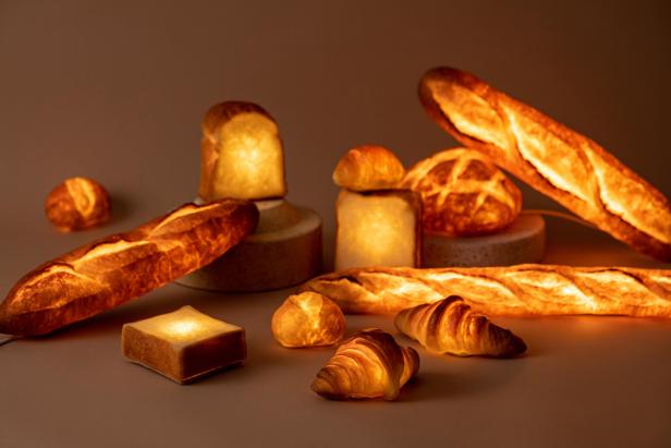Verschiedene Brotsorten und Croissants leuchten warm auf einer neutralen Oberfläche.