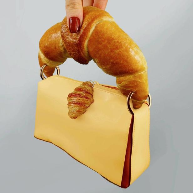 Ein Croissant dient als Griff für eine gelbe Handtasche, an der ein Mini-Croissant befestigt ist.