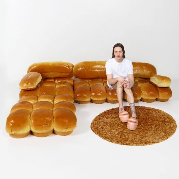 Ein Mann sitzt auf einem Sofa aus Brötchen, mit einem Teppich, der wie ein Burger aussieht.