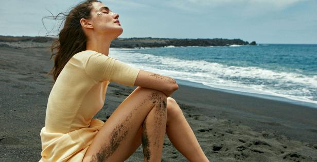 Eine Frau sitzt am Strand mit schwarzem Sand und genießt die Sonne.