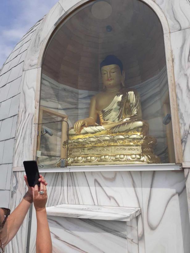 Eine Person fotografiert eine goldene Buddha-Statue in einem Schrein.