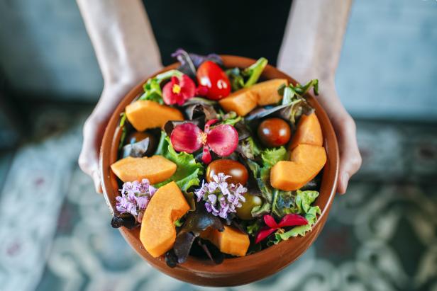 Eine Person hält eine Schüssel Salat mit Kürbis, Tomaten und essbaren Blüten.
