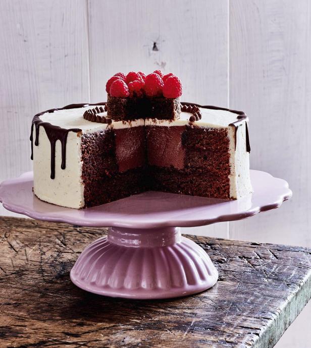 Ein angeschnittener Schokoladenkuchen mit Himbeeren auf einem rosa Tellerständer.
