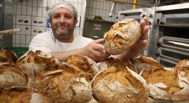 Ein Bäcker präsentiert frisch gebackenes, rustikales Brot in seiner Backstube.