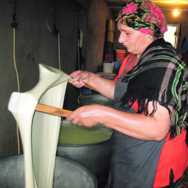 Eine Frau mit Kopftuch zieht Käse über einem Bottich.