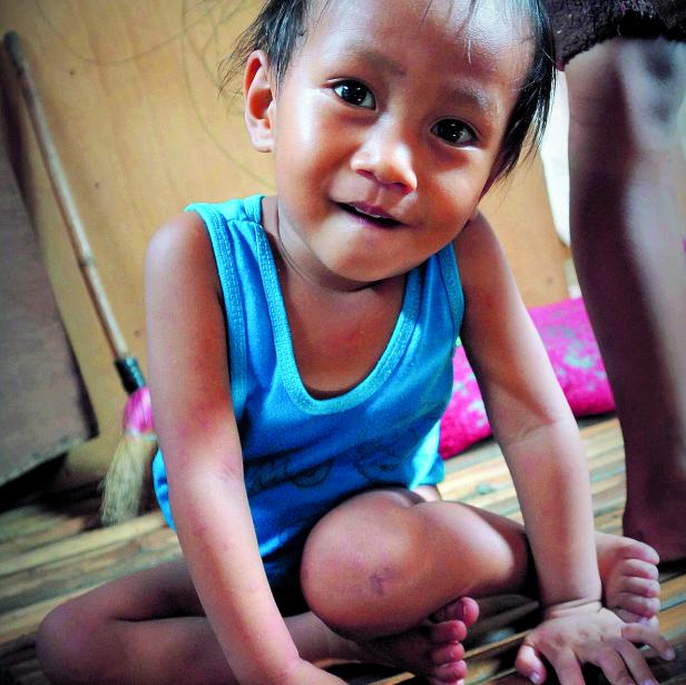 Ein lächelndes Kind sitzt auf dem Boden und trägt ein blaues Tanktop.