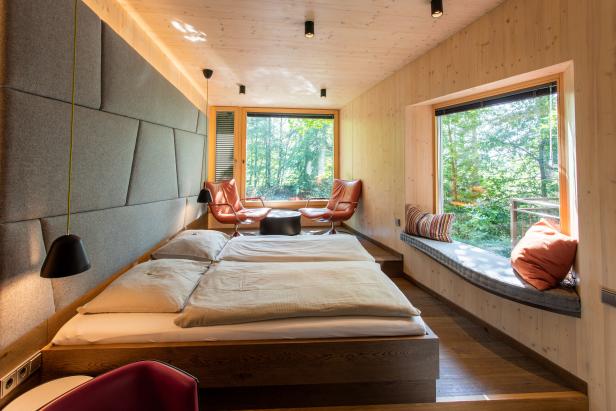 Ein Schlafzimmer mit Holzwänden und großen Fenstern mit Blick auf den Wald.