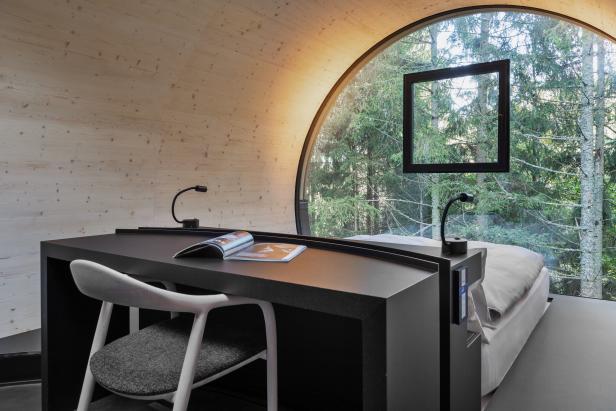 Ein modernes Zimmer mit Schreibtisch, Stuhl und Blick auf den Wald.