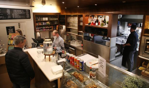 In einem Café bestellt ein Kunde an der Theke, hinter der ein Mitarbeiter mit Maske steht.