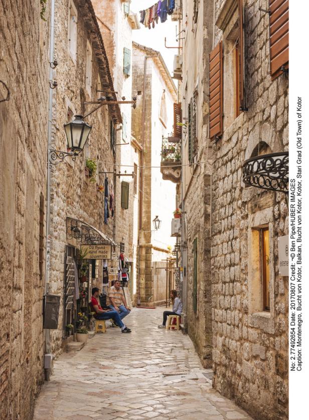 In einer Gasse in Kotor sitzen Menschen vor einem Souvenirladen.
