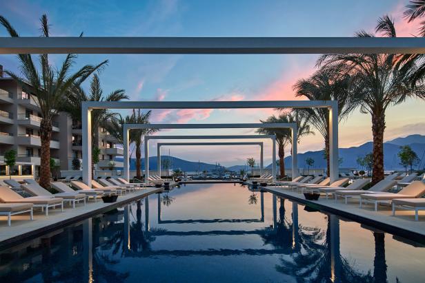Ein luxuriöser Poolbereich mit Palmen und Blick auf einen Yachthafen bei Sonnenuntergang.