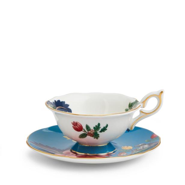 Eine bemalte Teetasse steht auf einer blauen Untertasse.