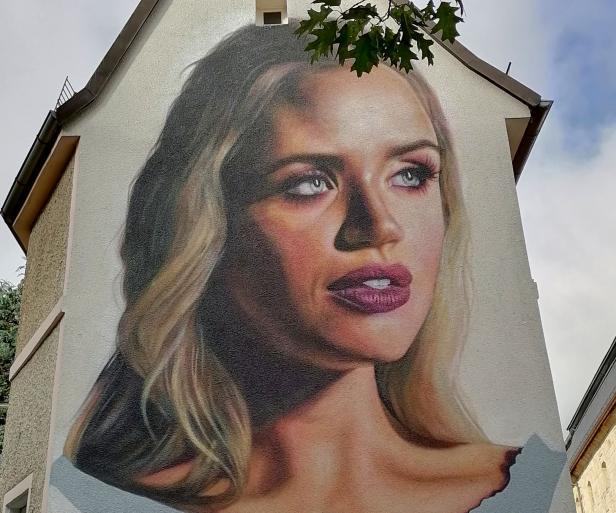 Ein Porträt einer Frau mit blonden Haaren ist auf eine Hauswand gemalt.