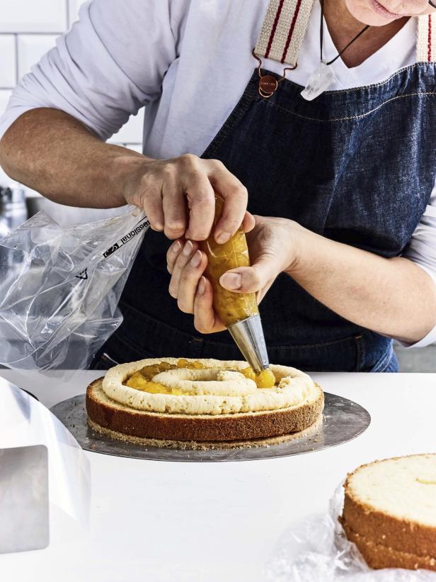 Eine Konditorin dekoriert eine Torte mit einer Spritztülle und gelber Füllung.