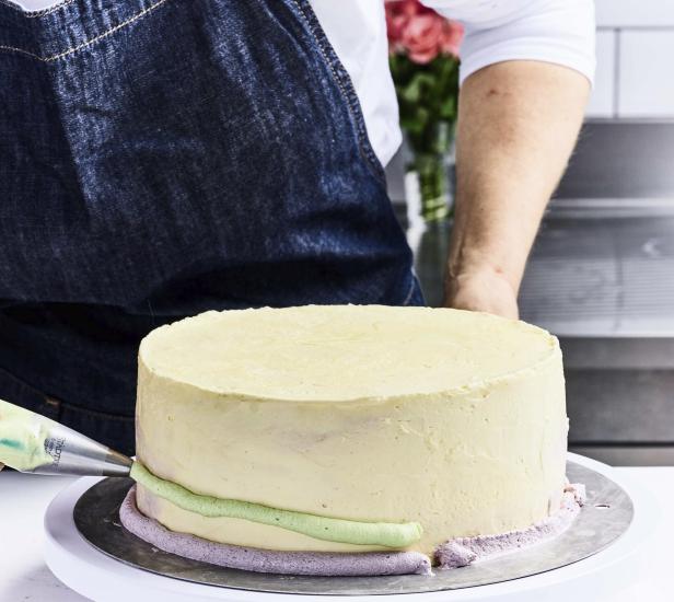 Eine Person verziert eine Torte mit grünem und lila Zuckerguss.