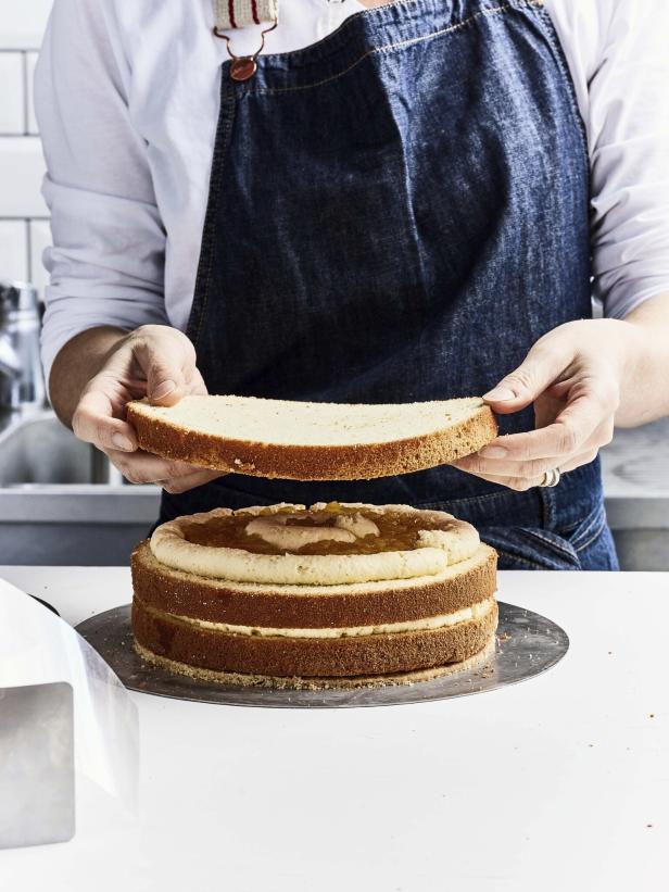 Eine Person setzt einen Tortenboden auf eine mehrschichtige Torte mit Füllung.